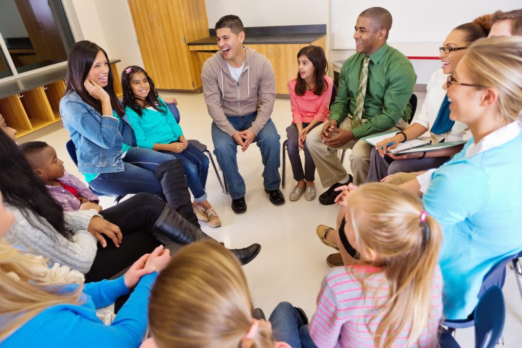 Parents meeting in a circle with kids for a parenting program.