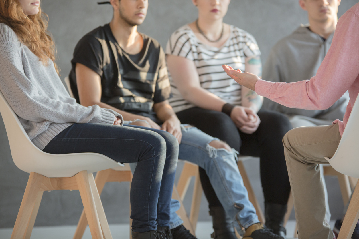 An instructor speaking with a group of teens sitting in chairs in a circle.