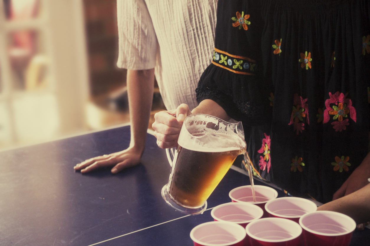 Teen girl pouring beer into disposable cups for a drinking game.
