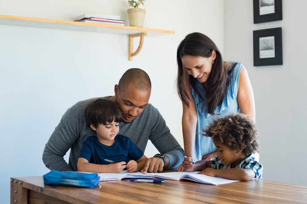 Happy family with two young kids doing homework at kitchen table