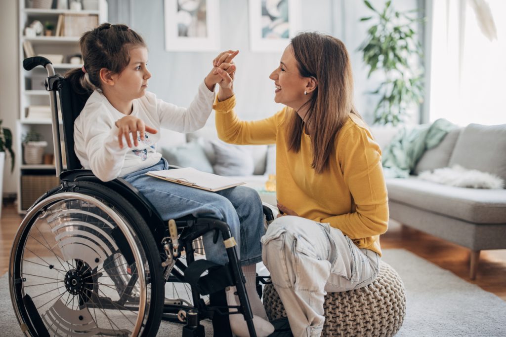 Mother and young daughter in wheelchair together in living room at home